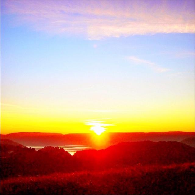 Solnedgang over en dal i det sola er i ferd med å synke bak fjellet.